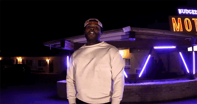 a man stands in front of a budweiser motel at night