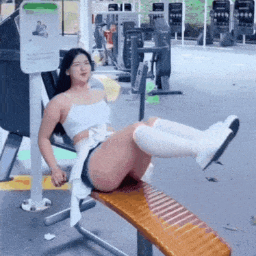 a woman is sitting on a bench in a gym with her legs up .