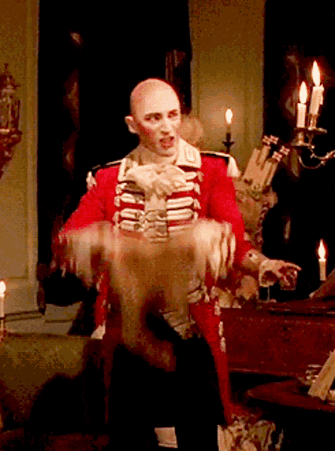 a bald man in a red and white uniform stands in front of a piano and candles