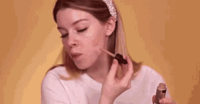 a woman wearing a headband is applying foundation to her face with a brush .