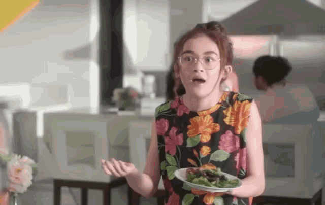 a girl in a floral dress holds a plate of food