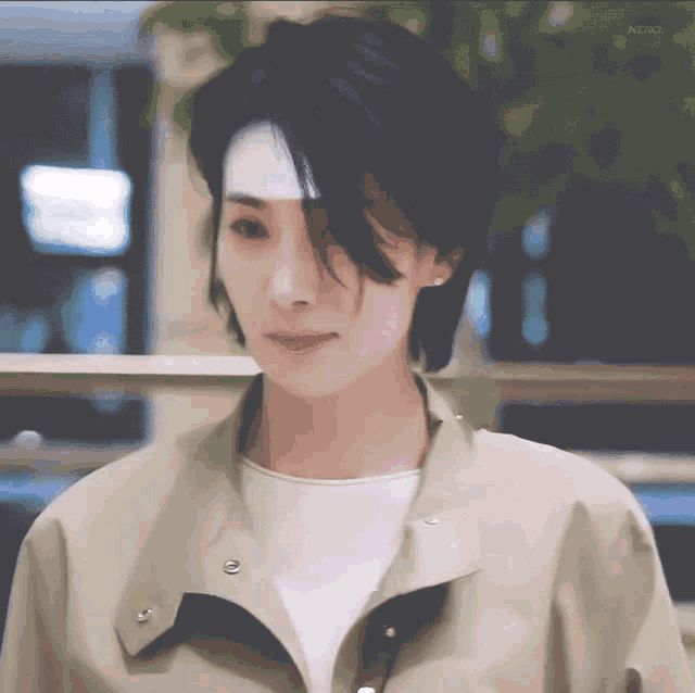 a woman with short black hair is wearing a tan jacket and white shirt .