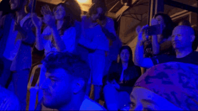 a group of people are sitting in a dark room with a blue light behind them