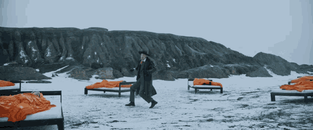 a man in a trench coat walks across a snowy field