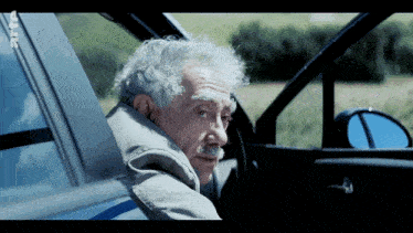 a man with gray hair and a mustache is sitting in a car with a sticker on the side that says rtl
