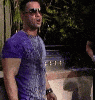 a man wearing sunglasses and a purple shirt is standing in front of a pool .