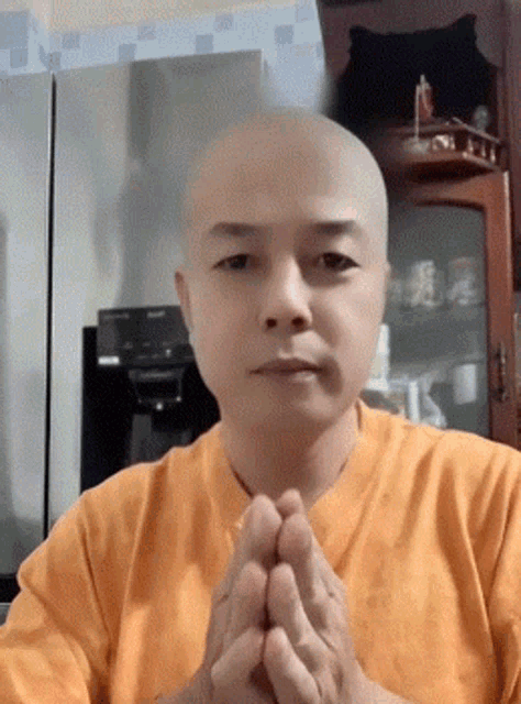 a bald man wearing an orange shirt is praying