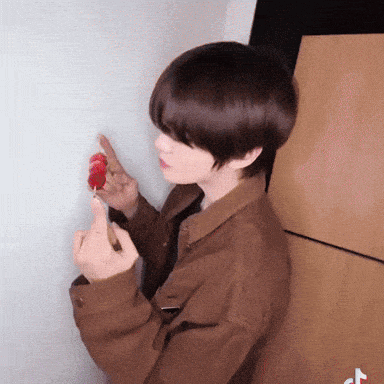 a person in a brown jacket holds a strawberry in their hand