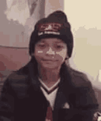 a young boy wearing a beanie and a jacket is sitting on a couch .