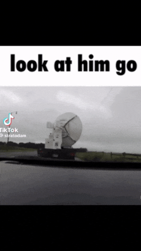 a truck with a large satellite dish on the back is driving down a road with the caption look at him go