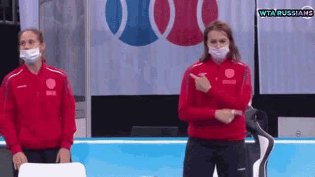 two women wearing face masks are standing in front of a wta russians sign