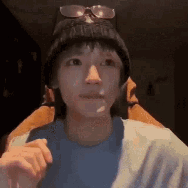 a young man wearing a beanie and sunglasses is looking at the camera .