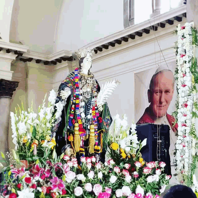 a statue in a church with flowers and a picture of a man