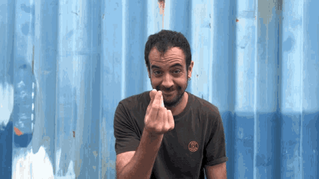a man wearing a t-shirt with a circle on it is giving the middle finger in front of a blue wall