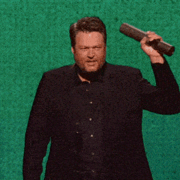 a man in a suit and black shirt is holding a microphone in front of a green background