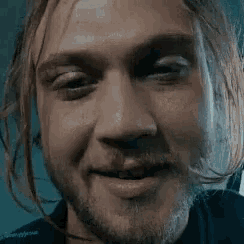 a close up of a man 's face with a beard and long hair smiling .