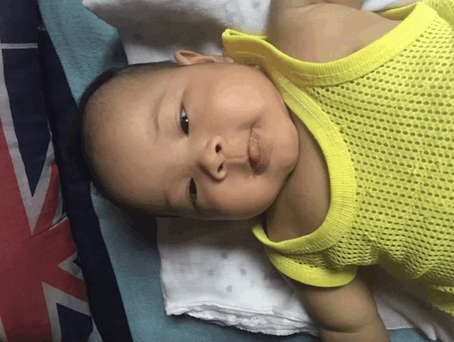 a baby wearing a yellow tank top is laying on a blanket