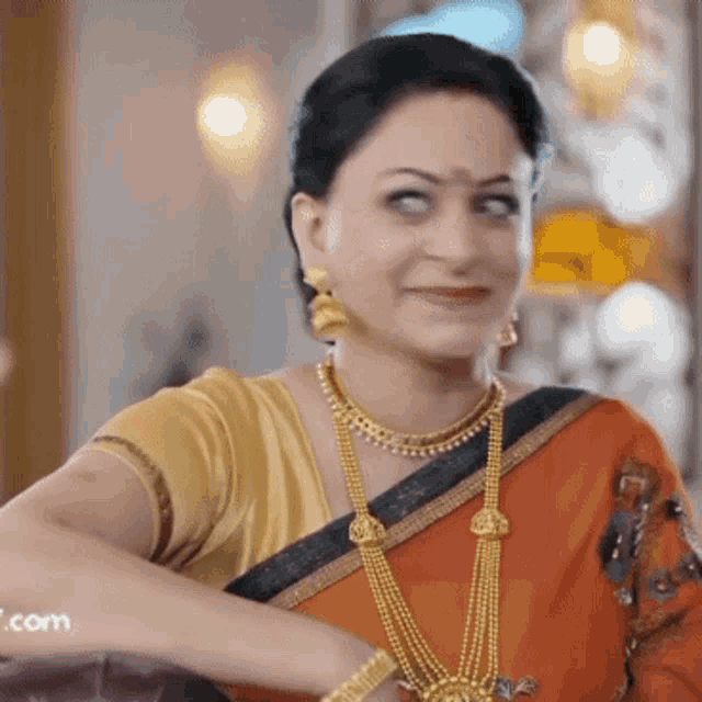 a woman wearing a gold necklace and earrings smiles