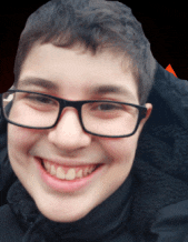 a boy wearing glasses and a black jacket smiles for the camera