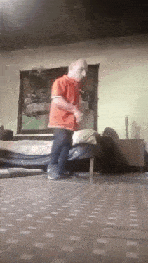 a man in an orange shirt is jumping on a bed
