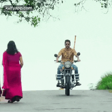 a man is riding a motorcycle down a road while a woman stands behind him .