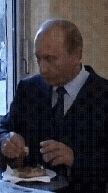 a man in a suit and tie is eating a sandwich with a fork