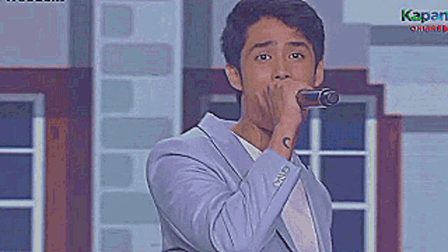 a man in a suit singing into a microphone with the word kapan on the bottom