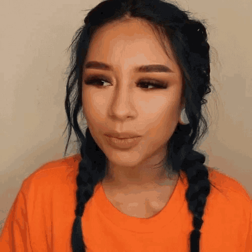 a woman with blue hair and braids is wearing an orange shirt and earrings .