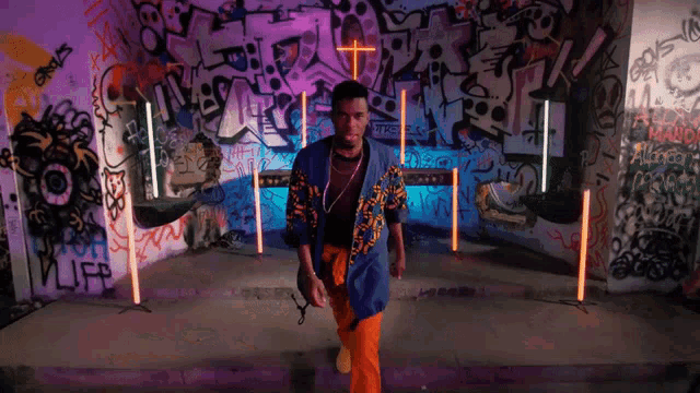 a man stands in front of a wall with graffiti on it and a cross