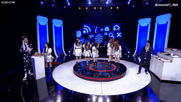 a group of girls are standing in a circle on a stage with a man in a suit behind them