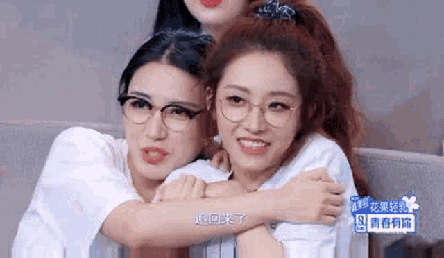 two women wearing glasses are hugging each other while sitting on a couch .