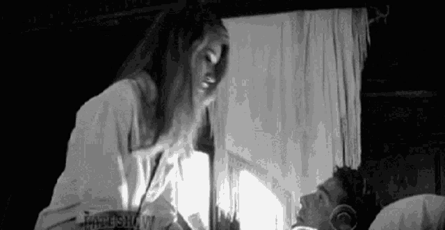 a woman is standing next to a man in a bed .