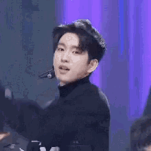 a young man wearing a black sweater and a microphone is standing in front of a blue wall .