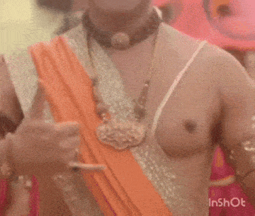 a shirtless man with a symbol on his forehead is smiling in front of a crowd of people .