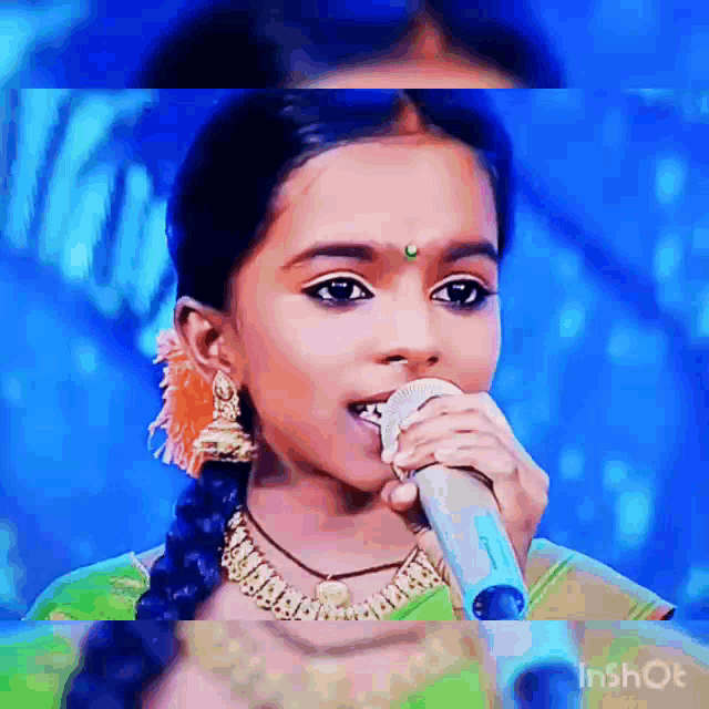 a little girl is singing into a microphone while wearing a green dress .