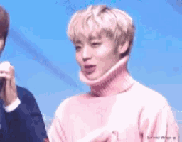 a man in a pink turtleneck sweater is holding a microphone .