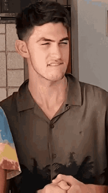 a young man wearing a shirt with palm trees on it is making a funny face