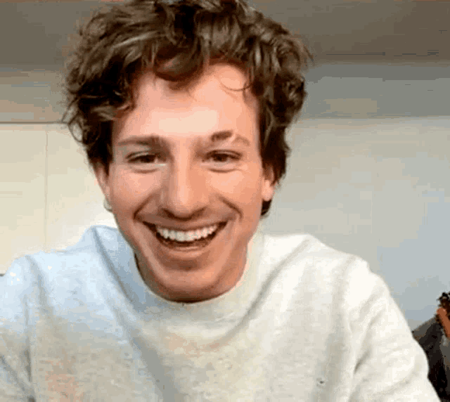 a man with curly hair is smiling for the camera while wearing a gray sweater .