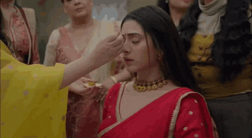 a woman in a red saree is getting her eyebrows done by a woman in a yellow dress .