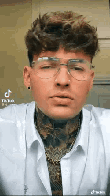 a man with glasses and a tattoo on his neck is wearing a white shirt and a gold chain .