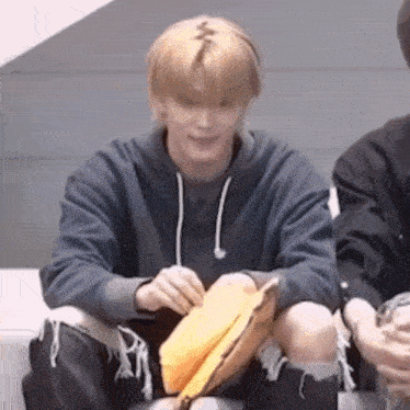 a young man is sitting on a couch holding a yellow bag and smiling .