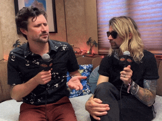 two men are sitting on a couch and one is holding a microphone that says ' abc ' on it