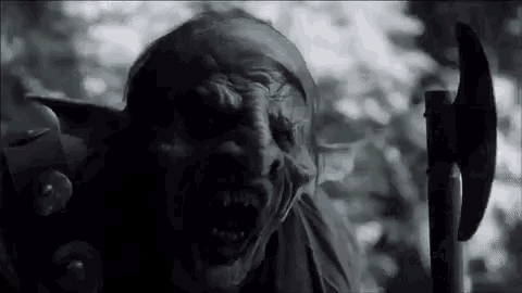a close up of a goblin holding an axe in a forest .