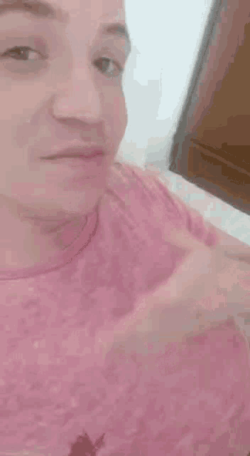 a man in a pink shirt is taking a selfie while sitting on a bed .