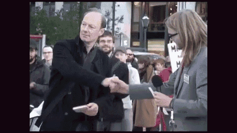 a man is shaking hands with a woman in front of a sign that says m.h.
