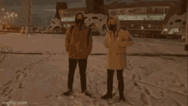 a couple of people standing in the snow at night .
