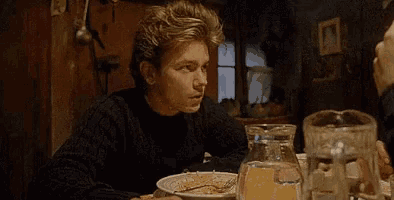 a young man is sitting at a table with a plate of food .