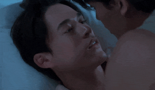 a man is kissing another man on the cheek in a bed