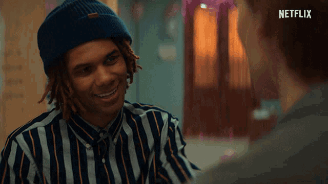a man wearing a blue beanie and a striped shirt is smiling in front of a netflix ad