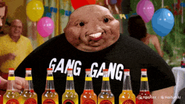 a man wearing a gang gang shirt stands in front of bottles of soda